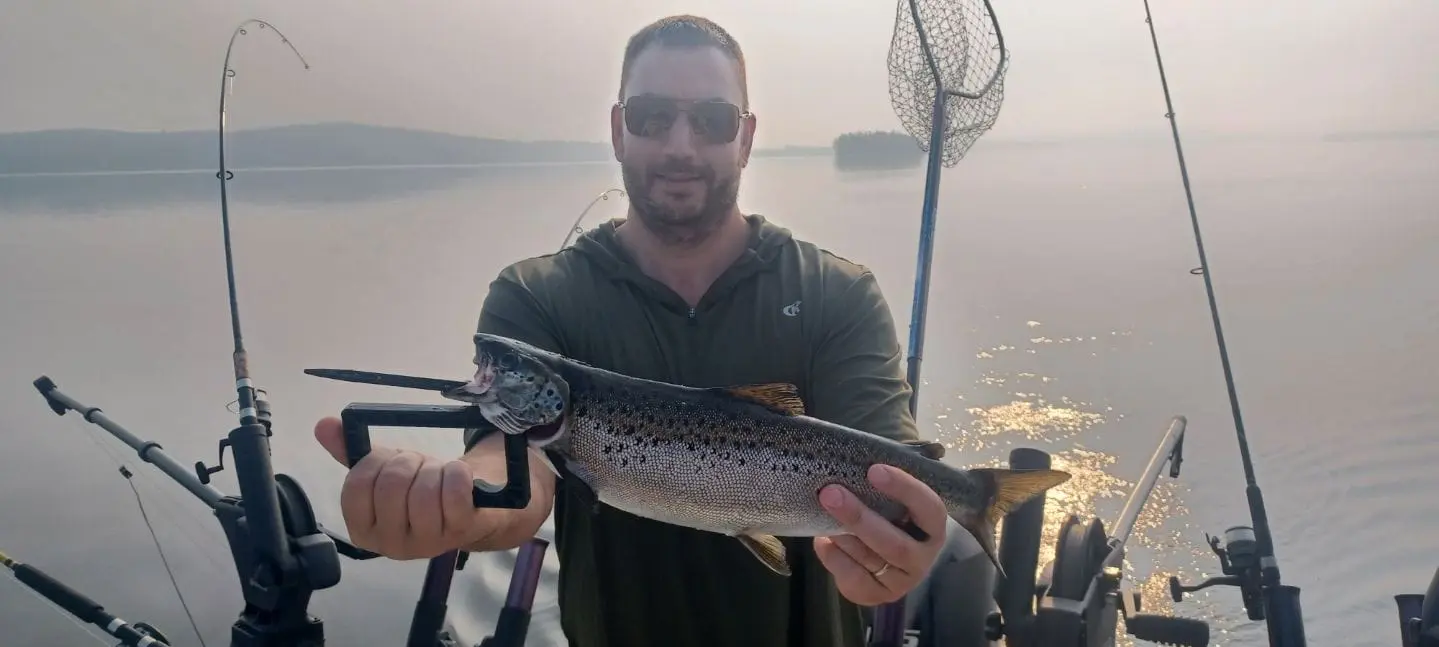 A man holding a Moosehead Lake Landlocked Salmon while standing at the back of Moosehead Area Guide Services Fishing Charter Boat
