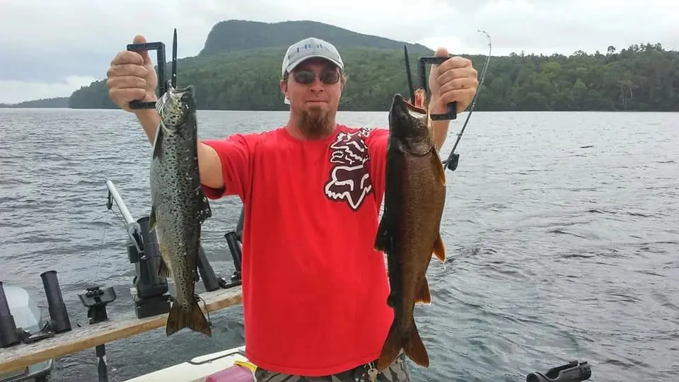 A man holding two fish on the water.