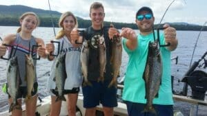 Four siblings on a boat holding up their freshly caught fish on a boat. Fishing Charter on Moosehead Lake